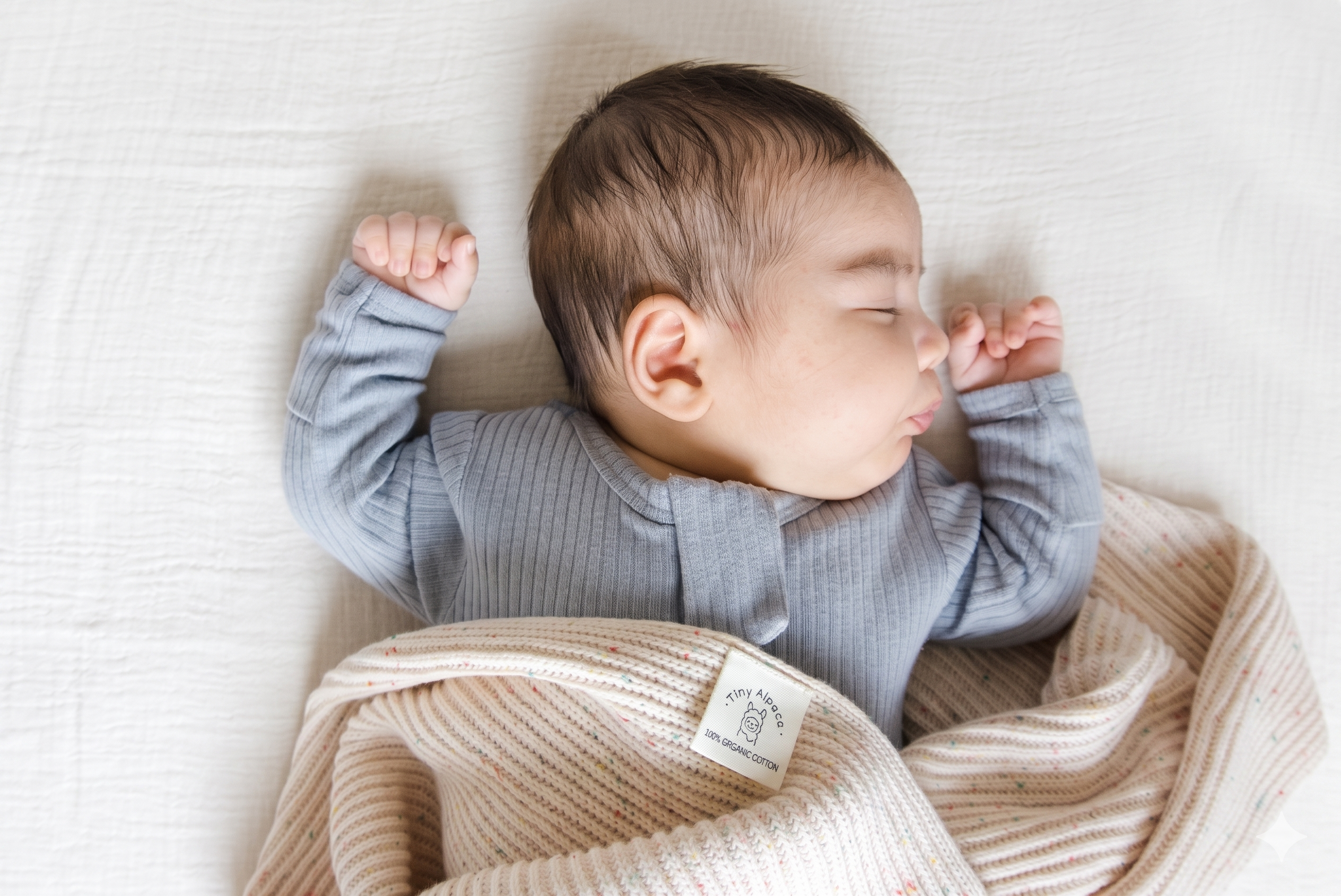 Baby wearing a soft ribbed sleepsuit while lying on a knitted blanket